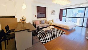 Una habitación de hotel moderna con zona de comedor, sofá, cama y un amplio ventanal con vista a la ciudad.
