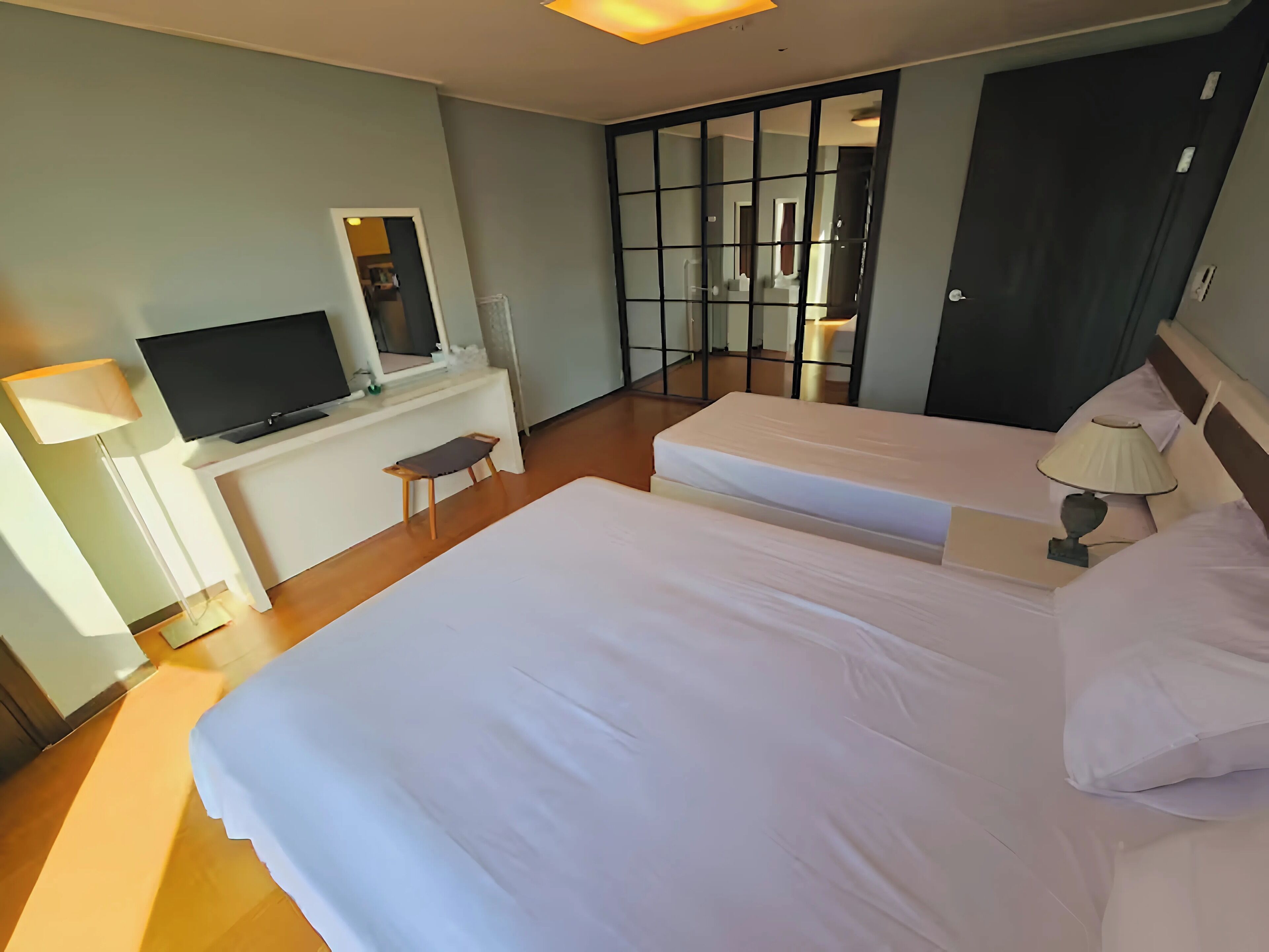 Une chambre d’hôtel avec deux lits, un bureau avec une télévision, une chaise et un grand miroir.