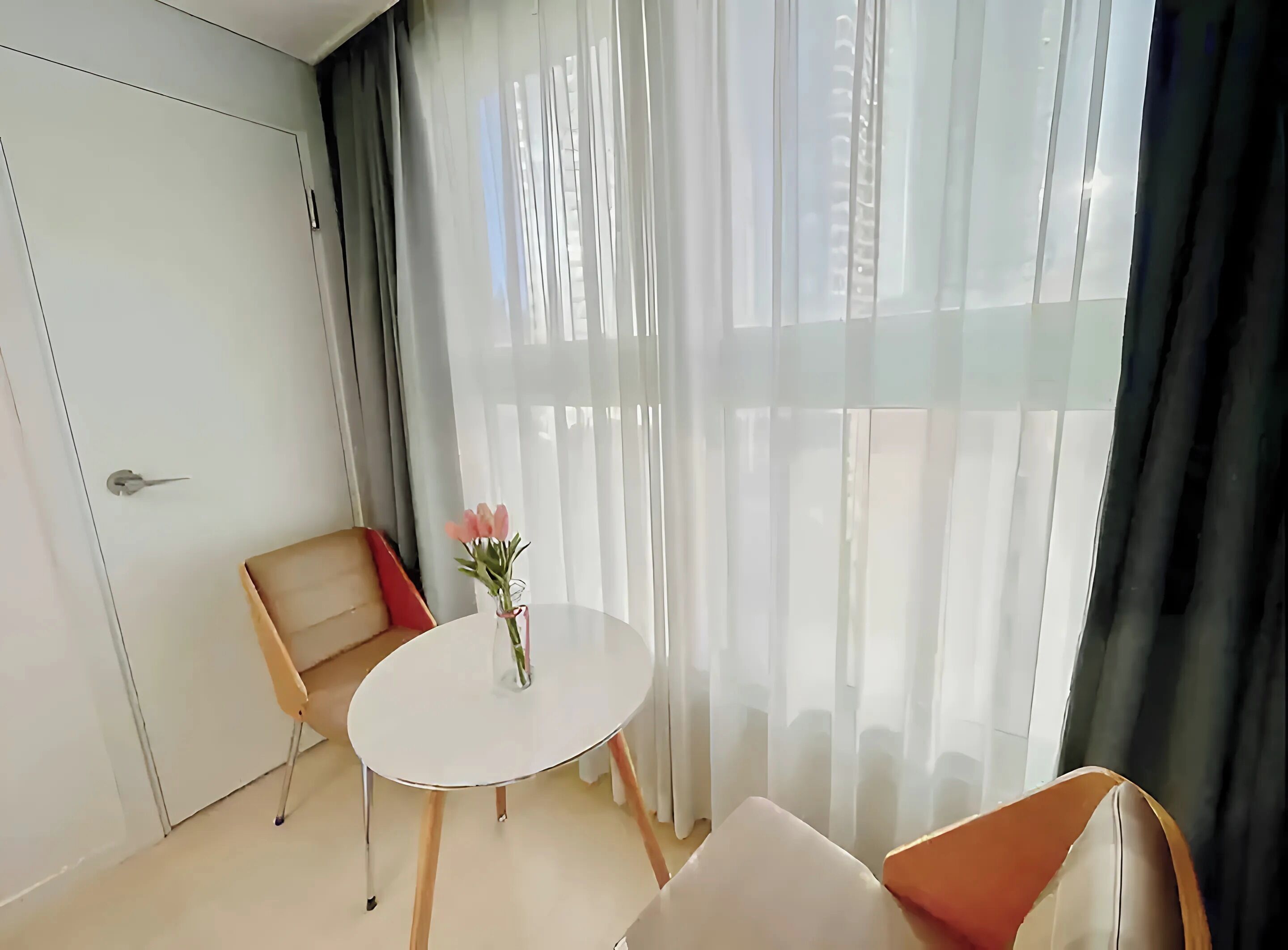 A modern room with a white door, a round table with a vase of flowers, and two chairs.