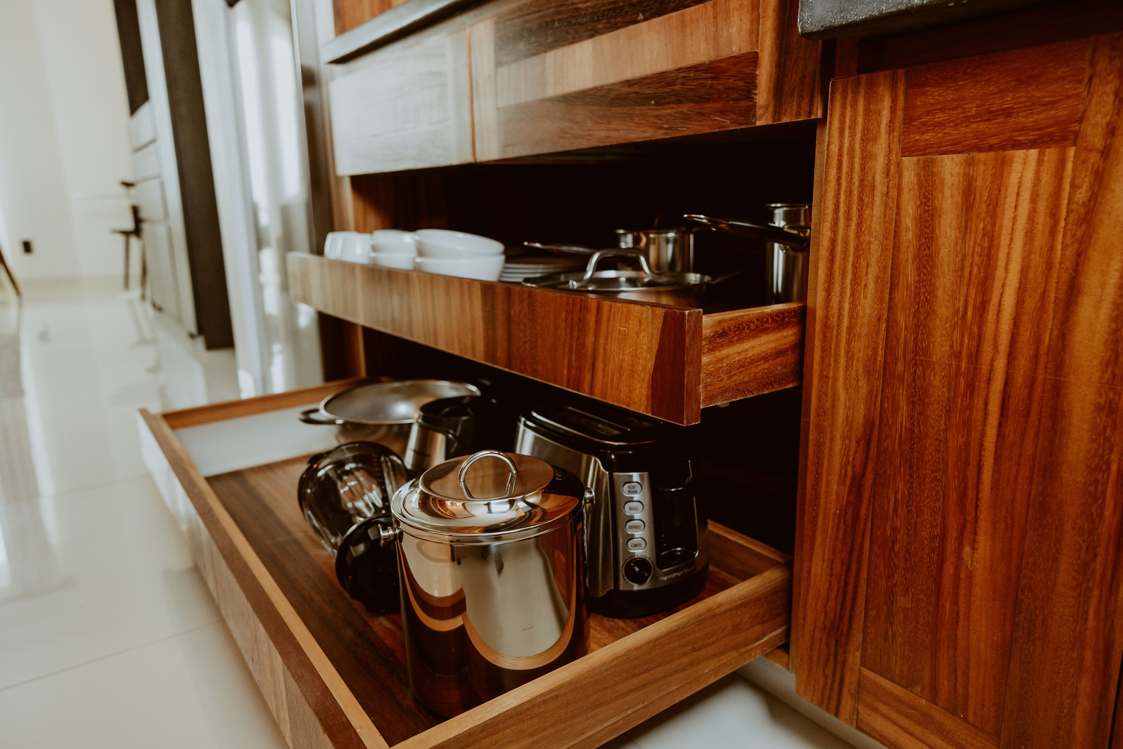 Una cocina con armarios de madera, un hervidor de acero inoxidable, una cafetera y una bandeja.