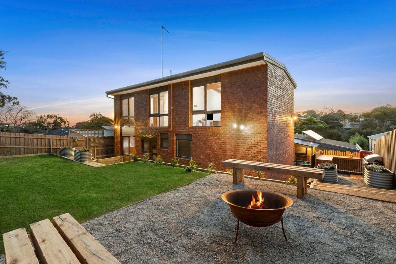 A modern house with a brick exterior, a well-maintained lawn, and a fire pit in the backyard.