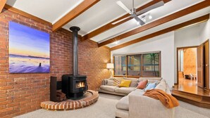 A cozy living room with a brick fireplace, a large painting, and a modern ceiling fan. - The Weekender With Spa Sleeps 11 (Ocean Grove)