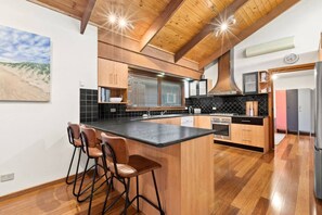 A modern kitchen with a central island, bar stools, wooden cabinetry, and a large window with blinds.