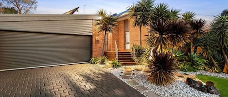 A modern house with a garage, a brick exterior, and a landscaped garden with various plants.