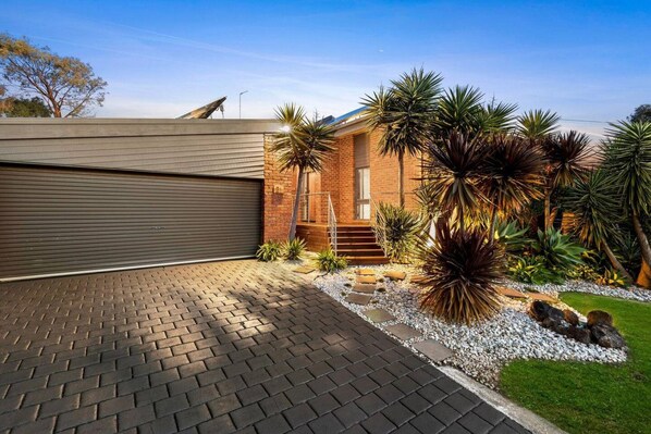 A modern house with a garage, a brick exterior, and a landscaped garden with various plants.