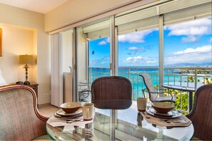 A balcony with a glass table set for two, overlooking a scenic ocean view.