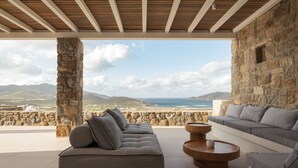 A modern outdoor seating area with a stone wall and a view of the sea and mountains. - Retreat Hill Luxury Villas Mykonos (Mykonos)