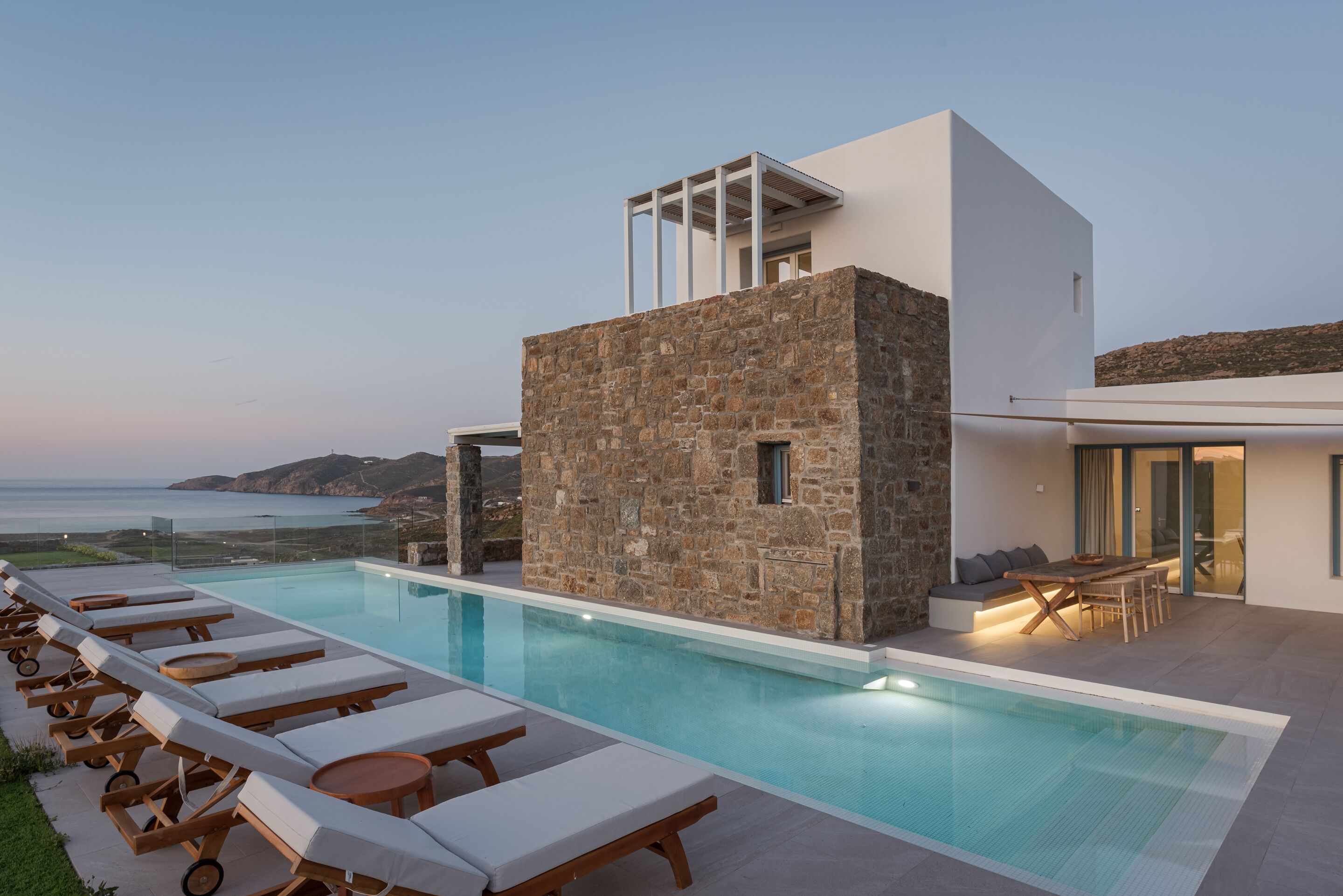 Ein moderner Poolbereich mit Liegestühlen, einer Steinstruktur und Blick aufs Meer.