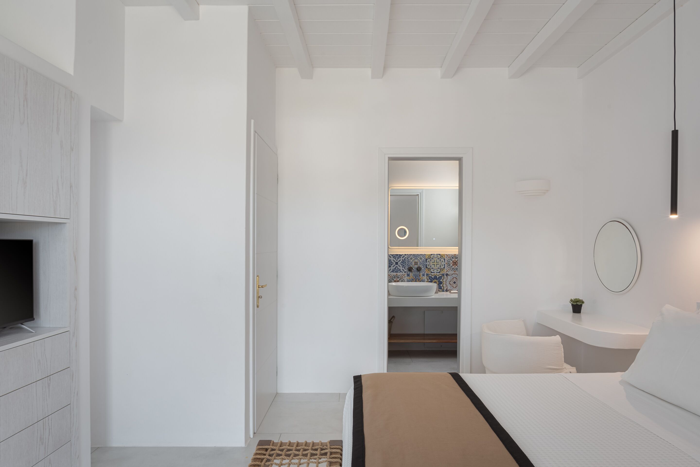 A modern hotel room with a large bed, a television, a bathroom with a mirror, and a small plant.