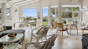 Une pièce spacieuse et bien éclairée, dotée d’un plafond haut, de grandes fenêtres offrant une vue sur l’extérieur, et de différents types de sièges, notamment un canap é, des fauteuils et une table à manger.