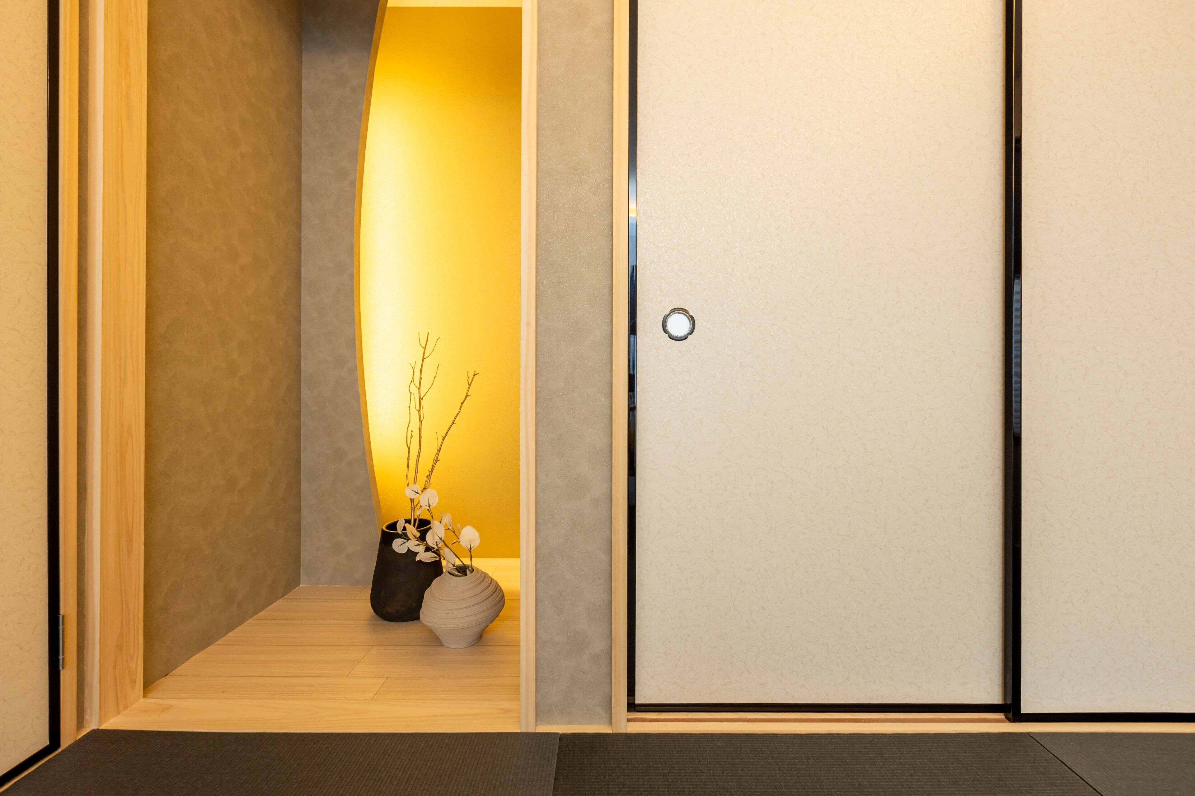 A hallway with a wooden floor, a door with a round handle, and two vases with branches on a yellow wall.