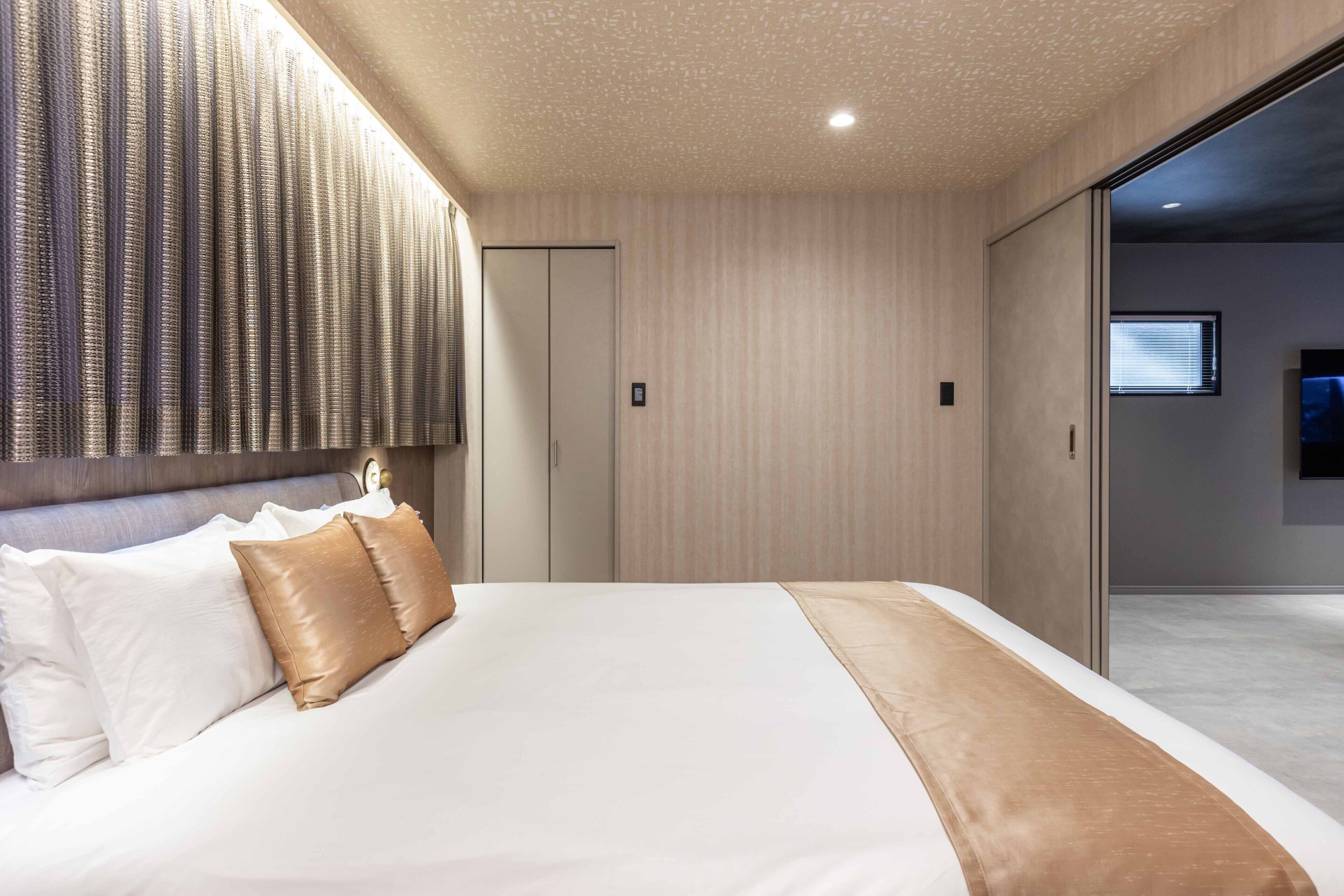 A modern hotel room with a large bed, a headboard with vertical lines, a sliding door closet, and a flat-screen TV mounted on the wall.