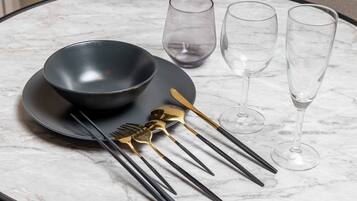 A table set with a black bowl, two wine glasses, and a set of cutlery including a gold spoon and black chopsticks.