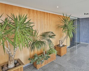 A modern lobby with wooden panel walls, potted plants, and a tiled floor.