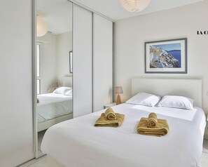 A hotel room with a large bed, a mirror, a framed picture on the wall, and a nightstand with a lamp.