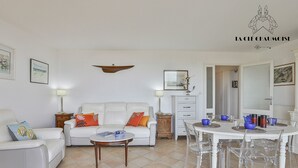 A living room with a white sofa, a coffee table, and a dining table with chairs. There is a small cabinet and a mirror on the wall.