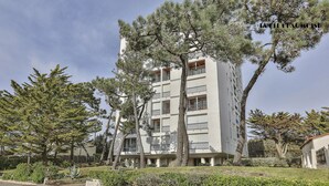 A multi-story building with balconies, surrounded by trees and greenery.