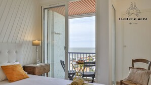 A hotel room with a bed, a nightstand, a lamp, a chair, and a balcony with a view of the sea.