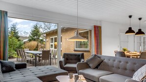 Un salon moderne avec un canapé d’angle gris, une table basse et un coin repas comprenant une table et des chaises.