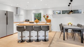 Une cuisine moderne dotée d’un îlot central, de tabourets de bar, d’une table à manger avec des chaises et d’un éclairage suspendu.