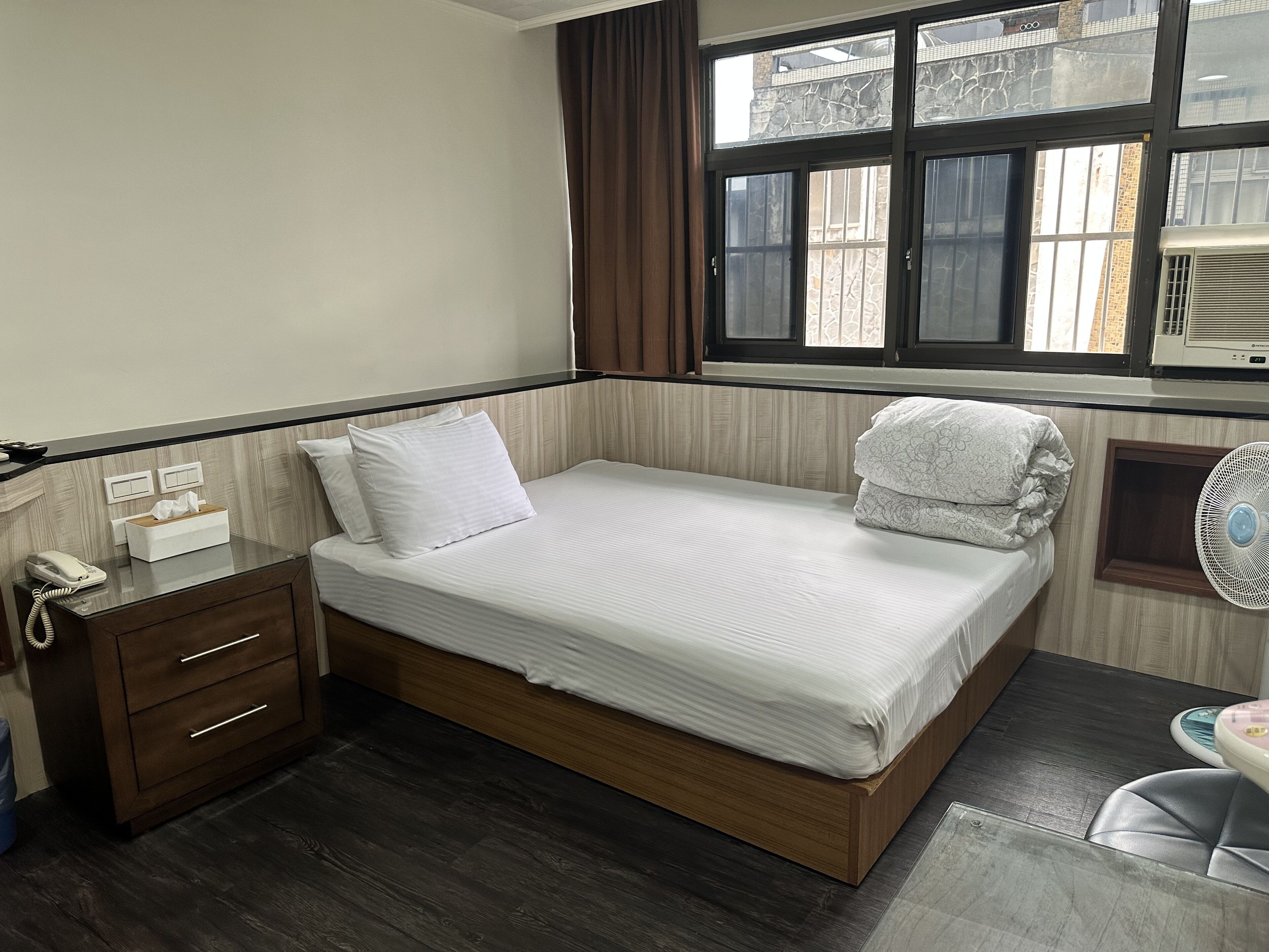 A single bed with a wooden frame, a bedside table with a phone, and a window with curtains.