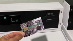 Une main tenant une carte de paiement devant un lecteur de carte.