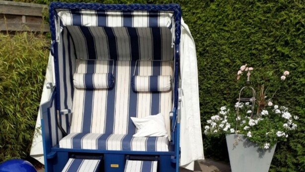 A blue and white striped outdoor lounge chair with a white cushion, positioned on a paved area with a green hedge in the background. - Vacation apartment Wenge, 1-2 pers. (Ascheberg-Davensberg)