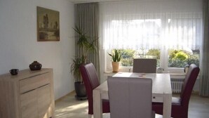 Zona de menjador amb taula i cadires, una planta en test, un quadre a la paret i una finestra amb cortines.