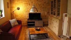 Ein Wohnzimmer mit Steinwand, einem roten Sofa, einem Couchtisch, einer Vitrine mit Glastüren und einem Fernseher.