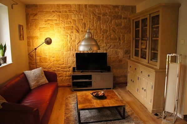 Un salon avec un mur en pierre, un canapé rouge, une table basse, un téléviseur et un meuble.