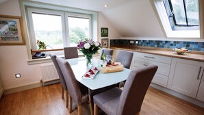 A dining area with a table set for four, a vase with flowers, and a bowl of fruit on the counter. - Owl Cote -  a cottage that sleeps 5 guests  in 3 bedrooms (Gatehouse of Fleet)