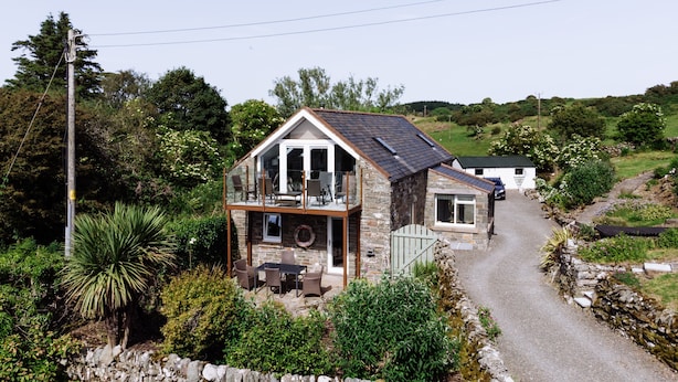 A two-story stone house with a balcony, a gravel driveway, and surrounding greenery. - Owl Cote -  a cottage that sleeps 5 guests  in 3 bedrooms (Gatehouse of Fleet)