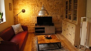 A living room with a stone wall, a red sofa, a coffee table, a cabinet with glass doors, and a television. - Ferienwohnungen Bisping33, Workershome 1-5 Pers (Ascheberg)