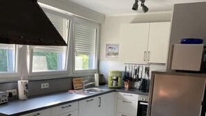A modern kitchen with white cabinets, a stainless steel refrigerator, and a dining area with a wooden table and chairs. - Ferienwohnungen Bisping33, Workershome 1-5 Pers (Ascheberg)