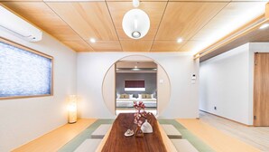 Een moderne hotelkamer met een houten plafond, een centrale houten tafel en zicht op een slaapkamer door een boog.