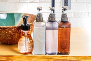 Four bottles of hair care products on a wooden surface with a ceramic bowl in the background. - JAPAVISTA Fuji (Osaka)