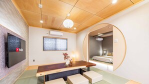 Een moderne hotelkamer met een houten plafond, een flatscreen televisie aan de muur, een houten eettafel met bankjes, een grote spiegel en een bed op de achtergrond.