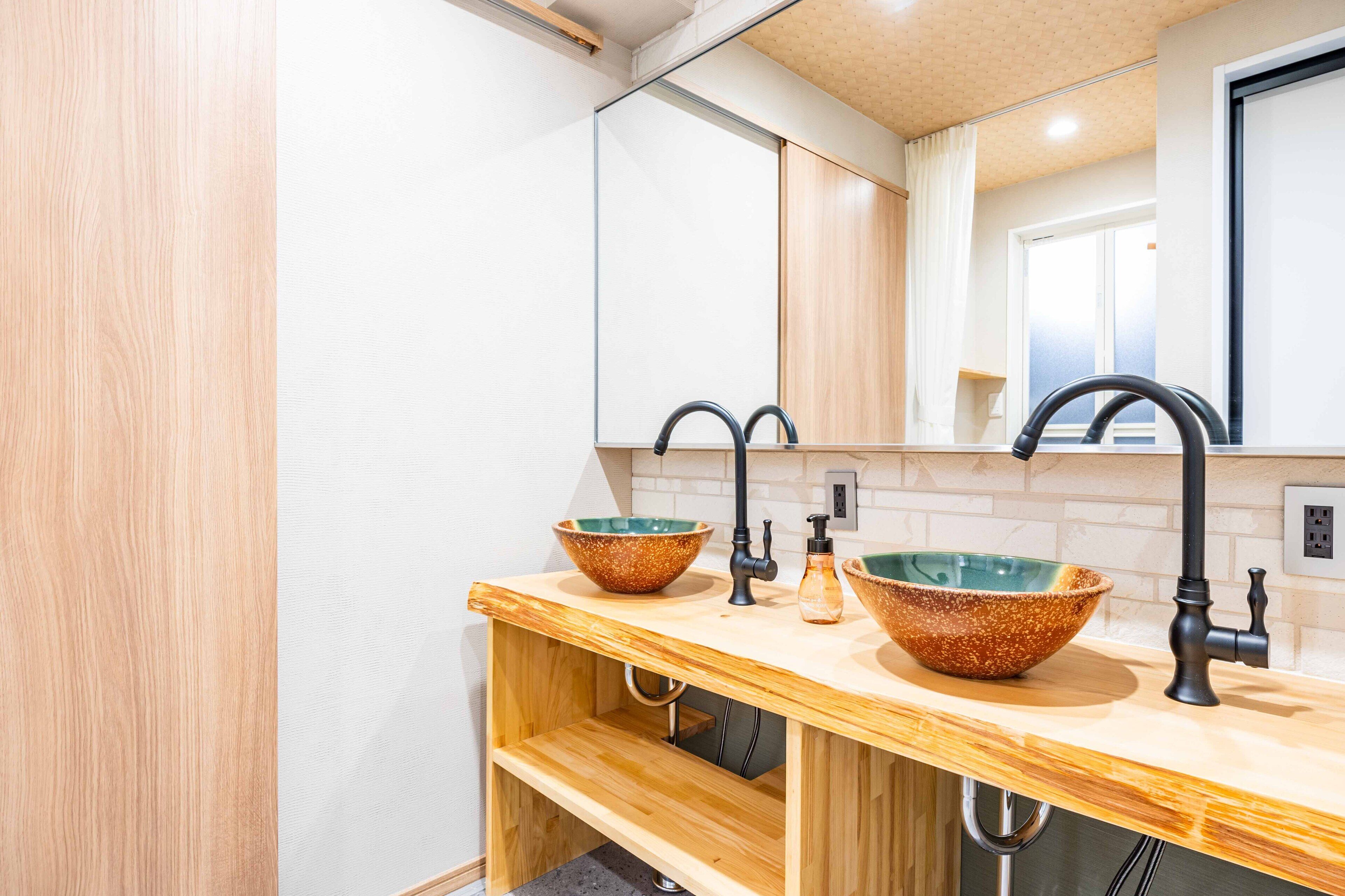 A modern bathroom with two ceramic bowls on a wooden vanity, a black faucet, and a mirror above the sink.