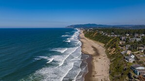Luchtbeeld van een kustgebied met een strand, huizen en heuvels op de achtergrond.