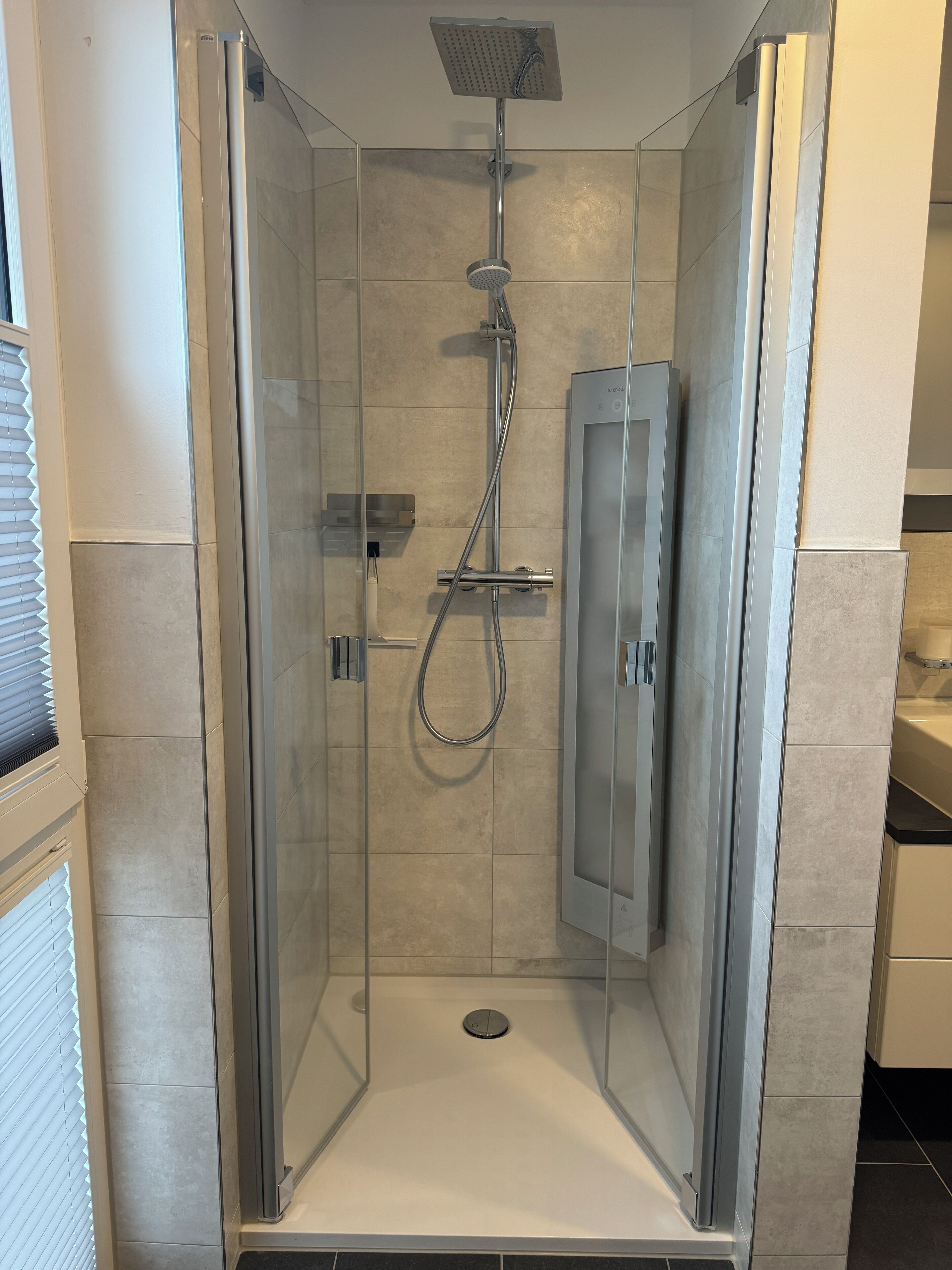 Een douchecabine met glazen wanden, een handdouche en een wandmengkraan.