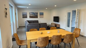 A modern living room with a sofa, a TV, and a dining area with a table and chairs. - Ferienhaus in Dreschvitz für bis zu 8 Personen (Dreschvitz)