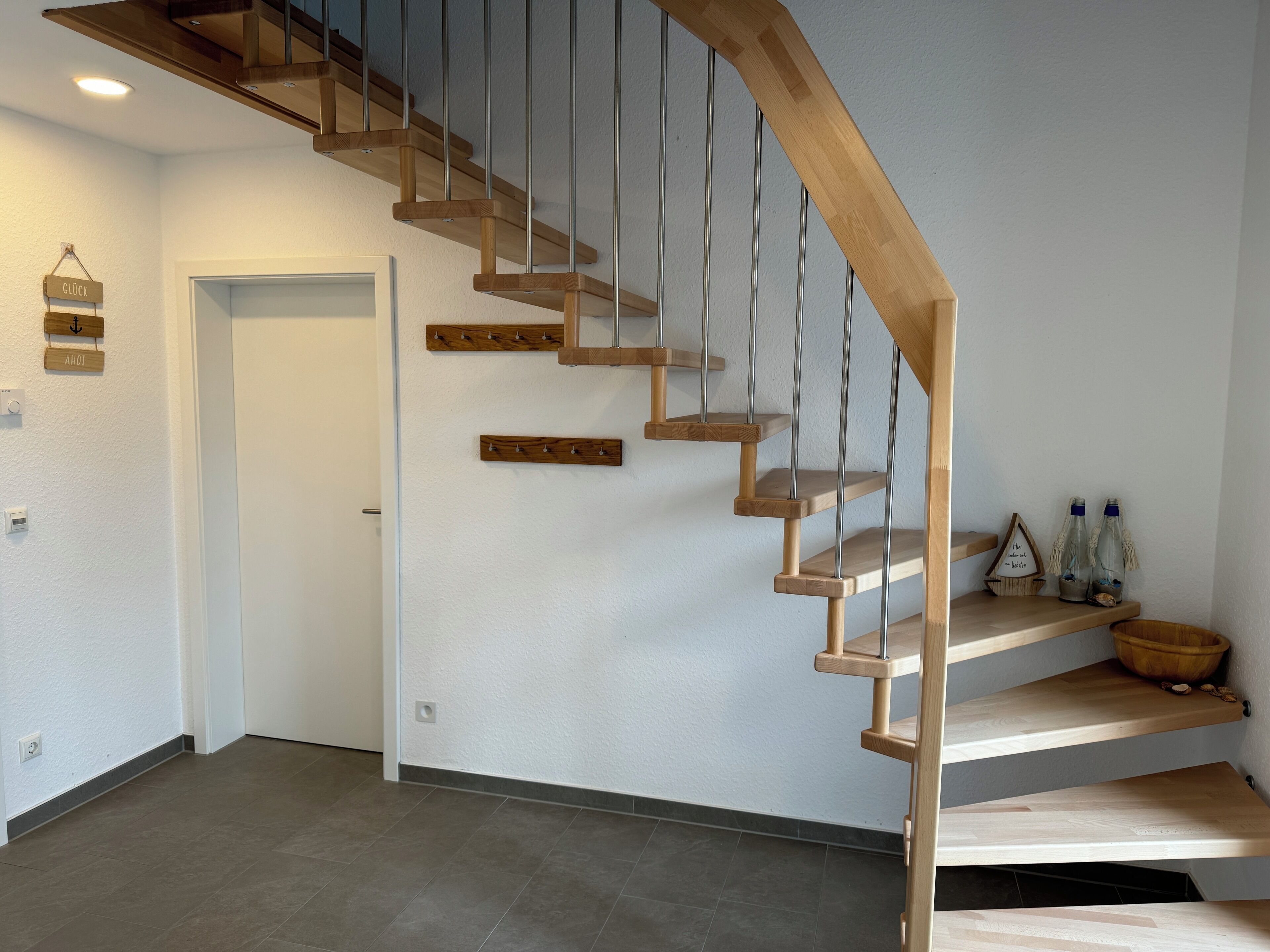 A wooden staircase with a handrail, a door at the bottom, and a shelf with decorative items.