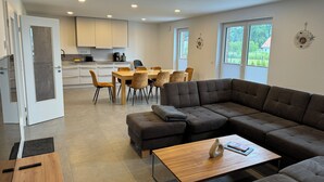 A modern living room with a sectional sofa, a wooden coffee table, and a dining area with a table and chairs. - Ferienhaus in Dreschvitz für bis zu 8 Personen (Dreschvitz)