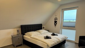 A bedroom with a large bed, a bedside table, a nightstand, a window with blinds, and a view of the outside. - Ferienhaus in Dreschvitz für bis zu 8 Personen (Dreschvitz)