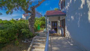 A house with a red-tiled roof, a covered porch, and a small table and chairs. - Cosy Apartment Rino, only 30m from the sea, island Pag (Košljun)