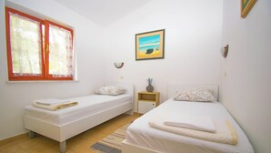 Two single beds with white linens, a window with curtains, a framed picture on the wall, and a small bedside table with a vase. - Cosy Apartment Rino, only 30m from the sea, island Pag (Košljun)