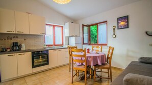 A compact kitchen with white cabinets, a built-in oven, and a dining area with a table and chairs. - Cosy Apartment Rino, only 30m from the sea, island Pag (Košljun)