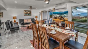 Ein modernes Wohnzimmer mit Essbereich, mit großem Fenster und Ausblick, Deckenventilator und Esstisch für zwei Personen.
