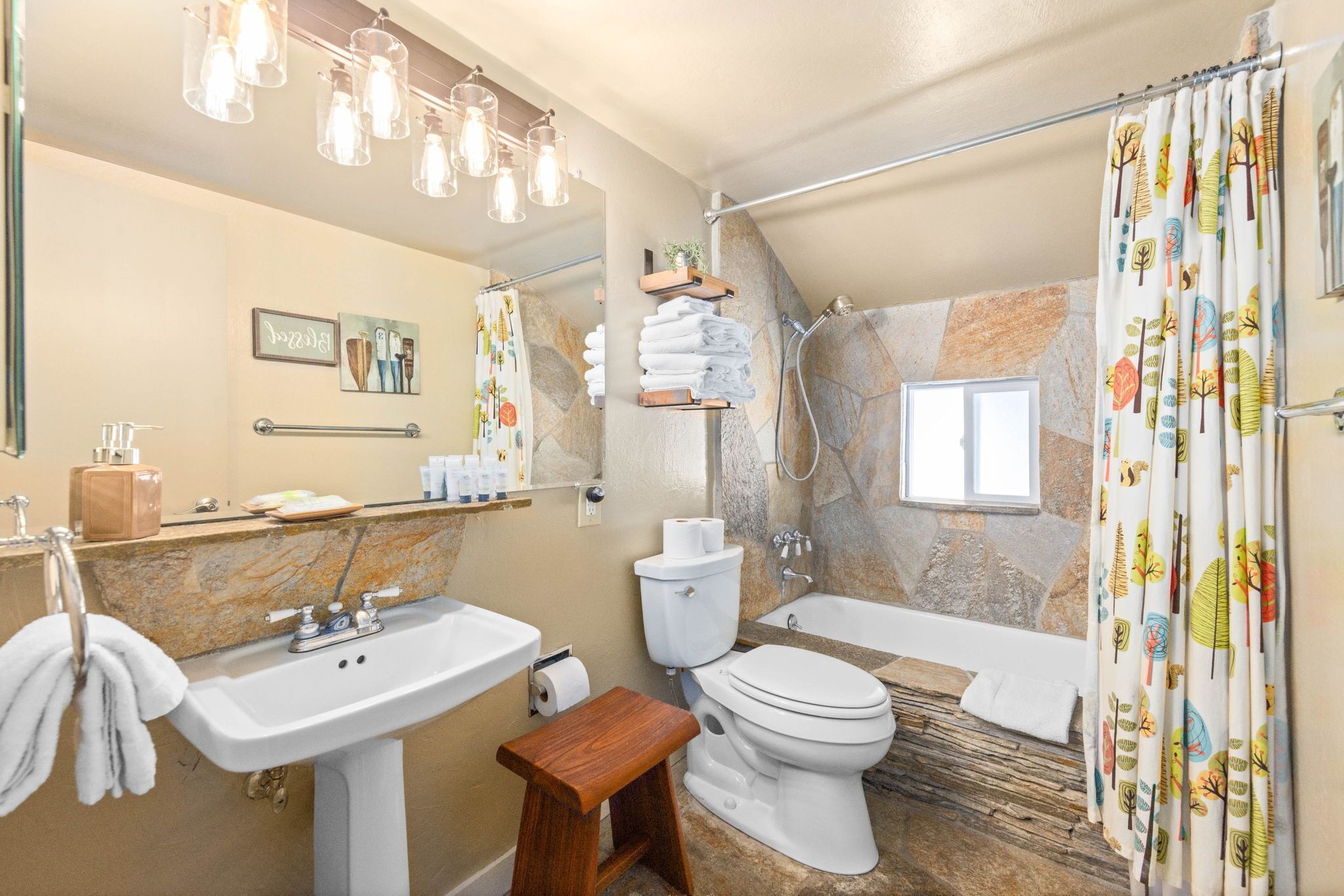 Ein Badezimmer mit Waschbecken, Toilette und Badewanne. Handtücher hängen an der Wand und ein hölzerner Hocker steht bereit.