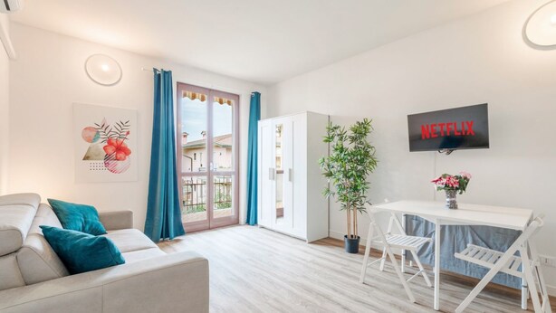 Un salon moderne avec un canapé, une table à manger et des chaises, une plante en pot et un téléviseur fixé au mur.
